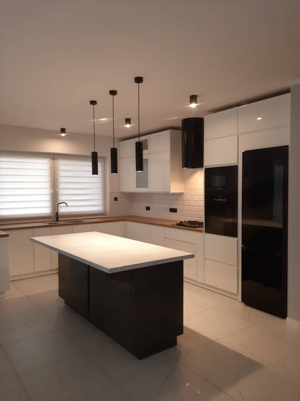 Nowoczesna kuchnia z wyspą: białe szafki, drewniany blat, czarne akcenty (okap, lampy, lodówka). Minimalistyczny design, płytki podłogowe, rolety w oknie.