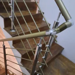 Nierdzewna balustrada schodowa z elementami w kolorze złotym, widok z góry, drewniane schody. Elementy łączone śrubami.