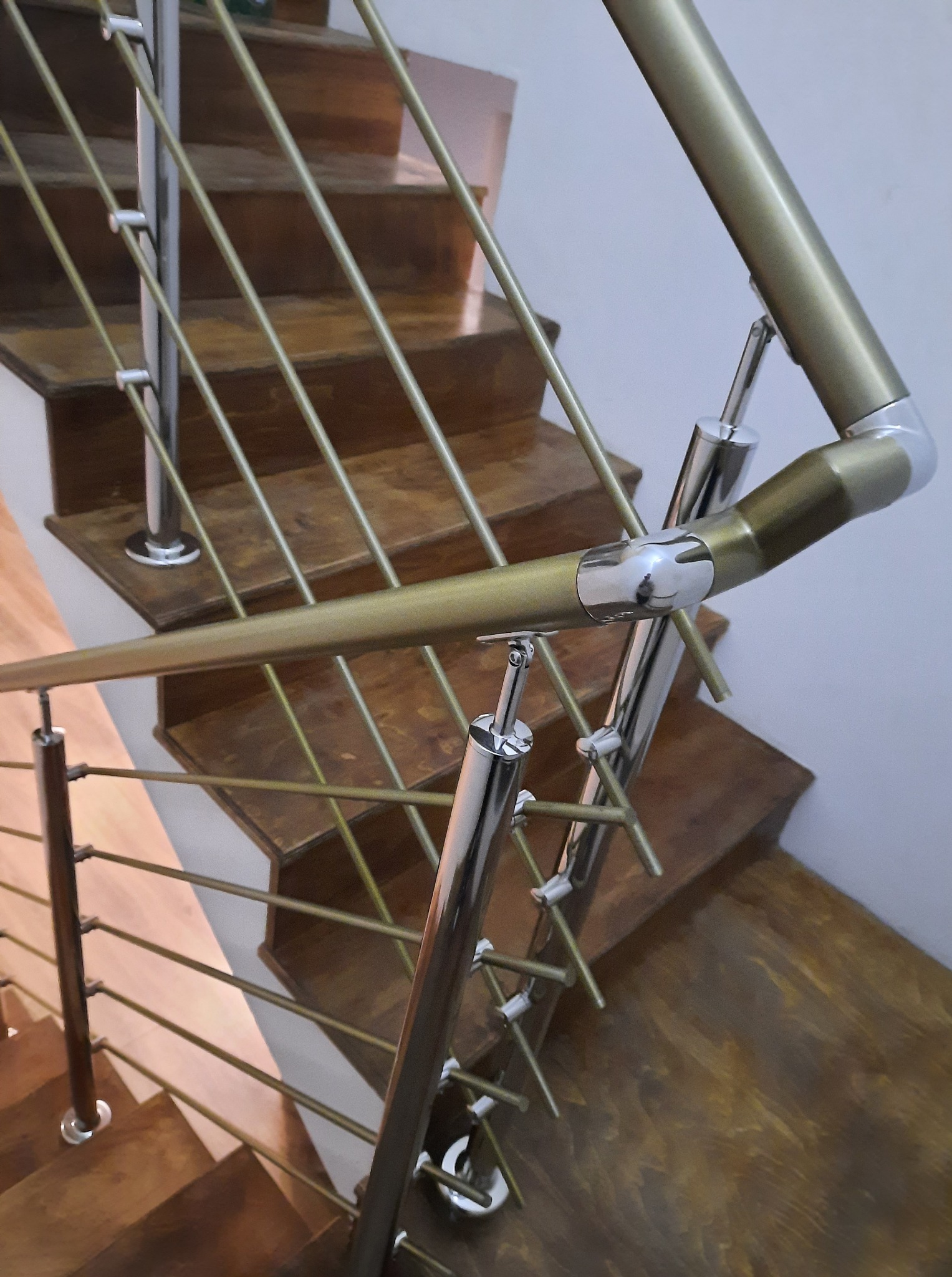 Nierdzewna balustrada schodowa z elementami w kolorze złotym, widok z góry, drewniane schody. Elementy łączone śrubami.