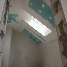 Kamil Gałka - Poddasze w trakcie prac wykończeniowych: szpachlowanie ścian i sufitu, widoczne okno dachowe. Fragment instalacji elektrycznej przy suficie. Surowy stan framugi.