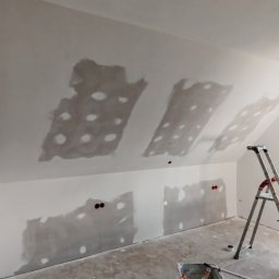 Kamil Gałka - Poddasze po szpachlowaniu w Stalowej Woli, widoczne ślady po łataniu dziur, drabina oparta o ścianę, okno z widokiem na zieleń. Przygotowanie do malowania.