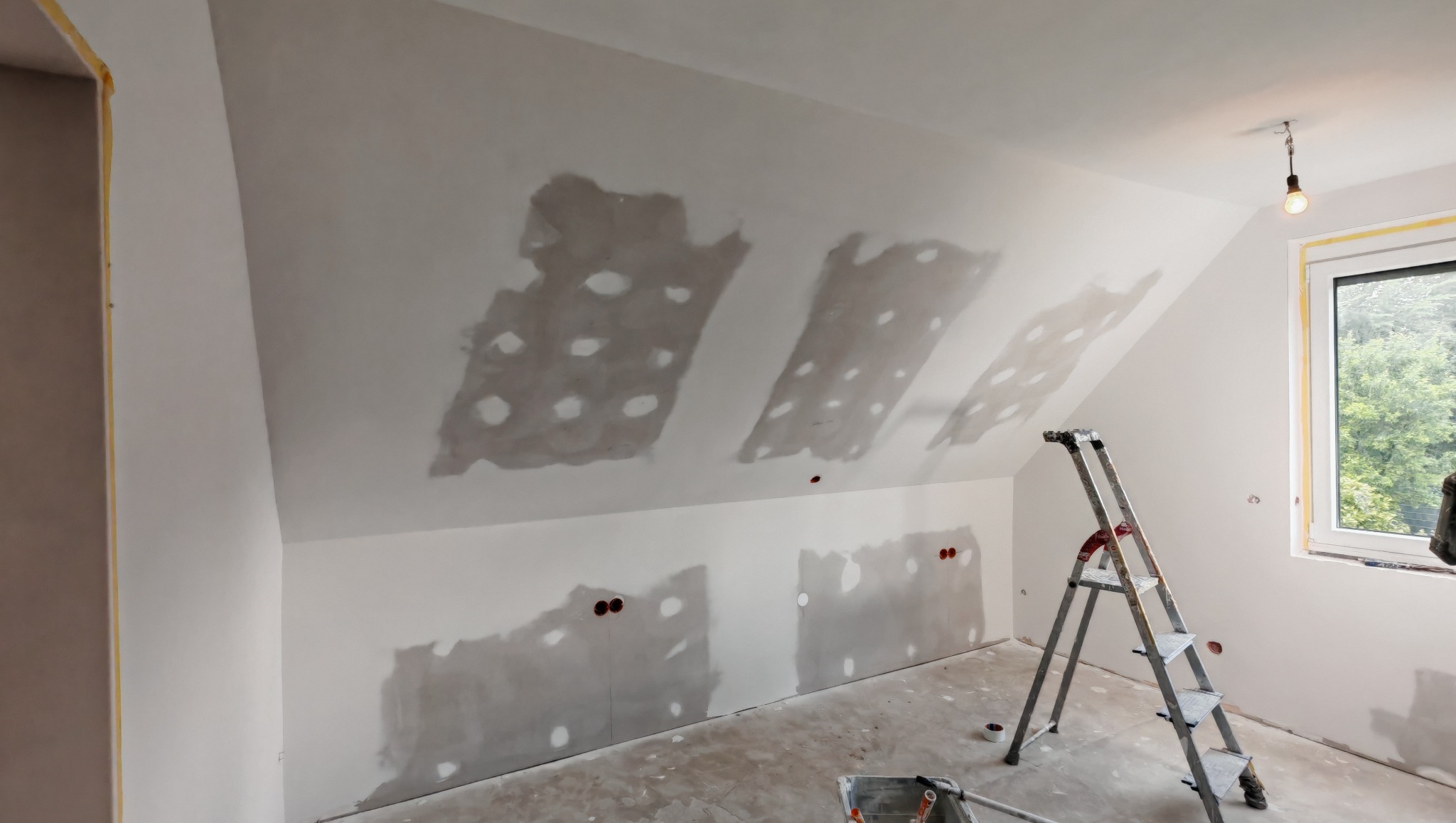Poddasze po szpachlowaniu w Stalowej Woli, widoczne ślady po łataniu dziur, drabina oparta o ścianę, okno z widokiem na zieleń. Przygotowanie do malowania.