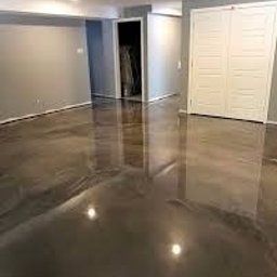 Art dekoracje microcement - Błyszcząca, szara posadzka żywiczna w pustym pomieszczeniu z białymi drzwiami i szarymi ścianami. Widoczne odbicia światła na gładkiej powierzchni podłogi.