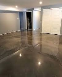 Błyszcząca, szara posadzka żywiczna w pustym pomieszczeniu z białymi drzwiami i szarymi ścianami. Widoczne odbicia światła na gładkiej powierzchni podłogi.