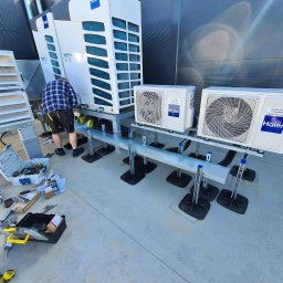 Najatek Air Grup - Montaż klimatyzacji Haier na dachu budynku. Widoczne jednostki zewnętrzne split, narzędzia pracy i instalator w trakcie podłączania. Szare tło dachu i elementy wentylacji.