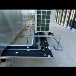 Instalacja rur w izolacji termicznej na zewnątrz budynku, poprowadzona w korytach kablowych. Widoczny agregat klimatyzacji i elementy konstrukcyjne dachu.