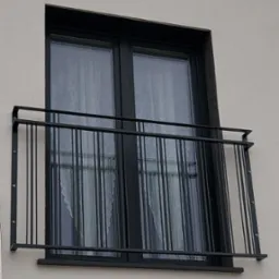 Czarna, metalowa balustrada okienna z pionowymi prętami, zamontowana na elewacji budynku. Widok na okno z firanką w tle, z zewnątrz.