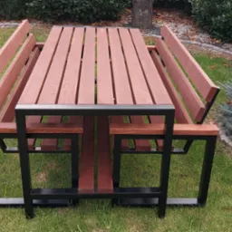 Stół piknikowy z drewna i metalu na trawie, otoczony zielenią. Stół z ławkami w nowoczesnym stylu, z czarną metalową ramą i drewnianymi elementami w ciepłym odcieniu brązu.