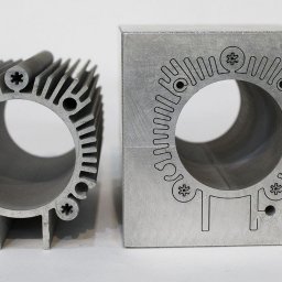 MetalTech EDM - Aluminiowe elementy po precyzyjnej obróbce: radiator z żebrami i blok z wygrawerowanym wzorem, oba z otworem w środku. Jasne tło.