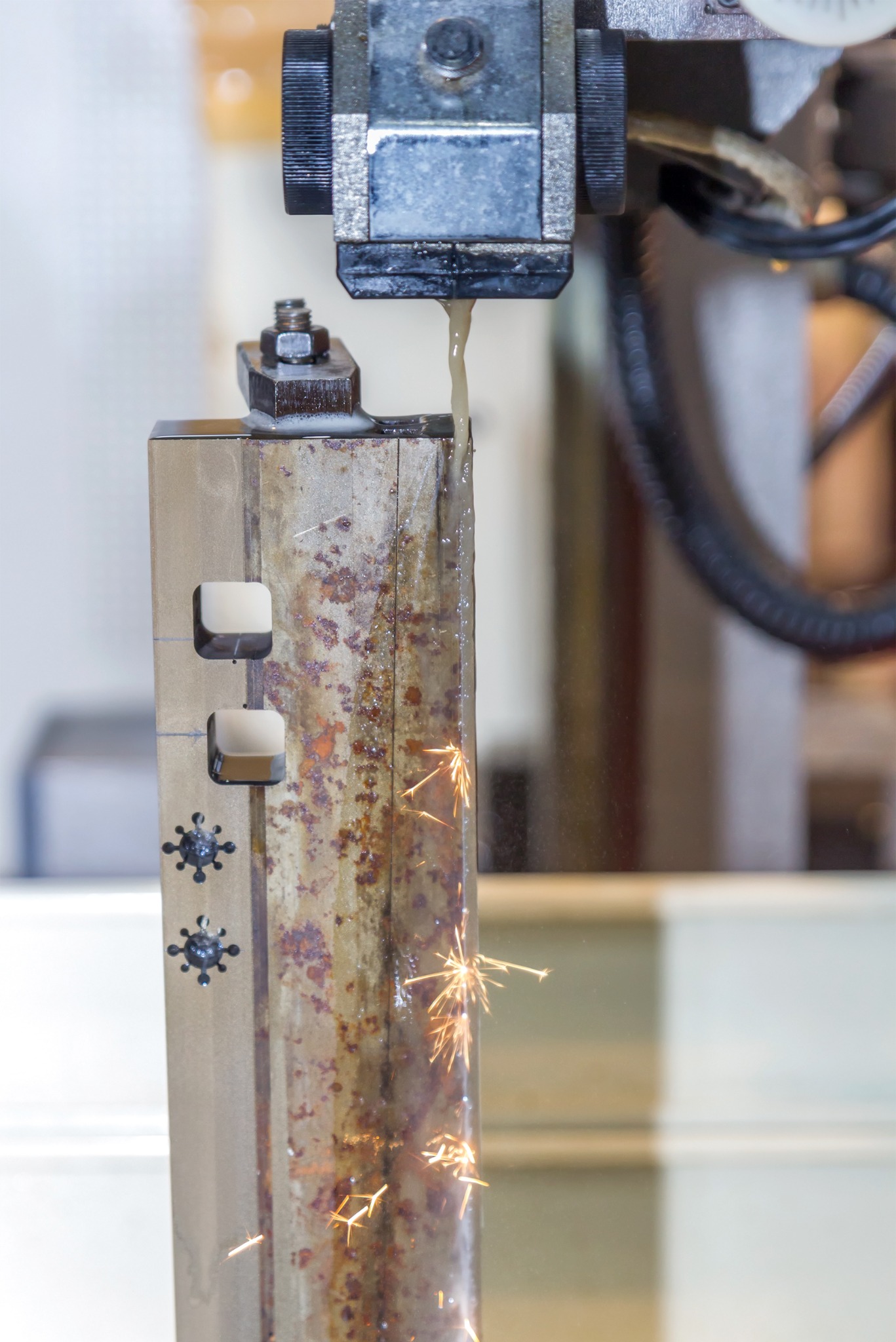 Elektroerozyjna obróbka metalu: iskry podczas cięcia wodą z dodatkiem oleju chłodzącego. Wycięte kwadratowe otwory i wzór na obrabianym elemencie ze śladami korozji.