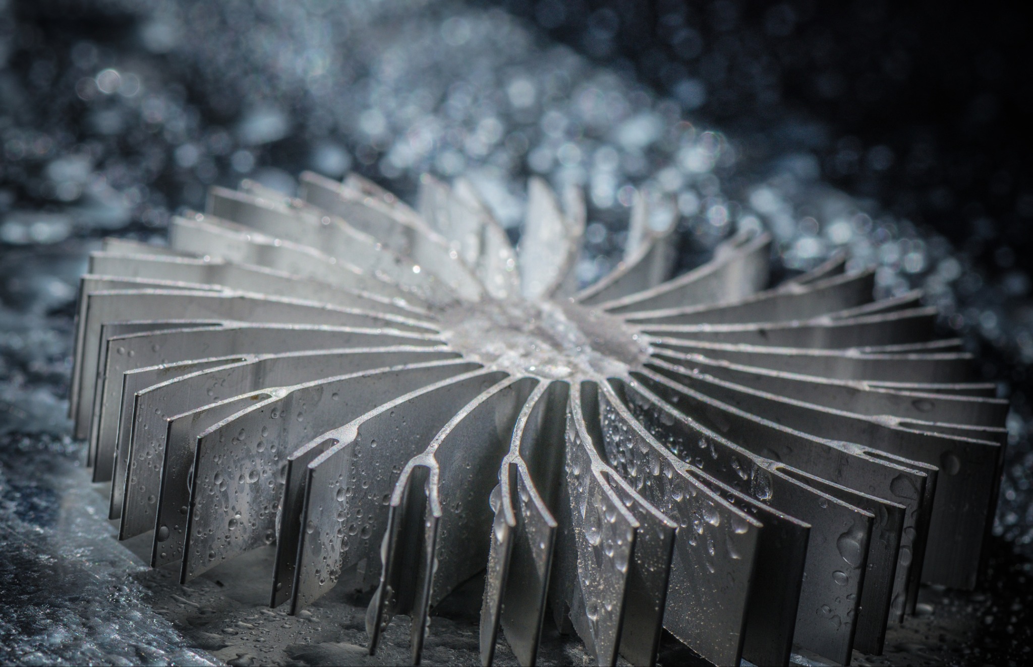 Metalowy radiator z precyzyjnie wyciętymi lamelami, pokryty kroplami wody, na rozmytym tle. Detal obróbki metalu, makro.