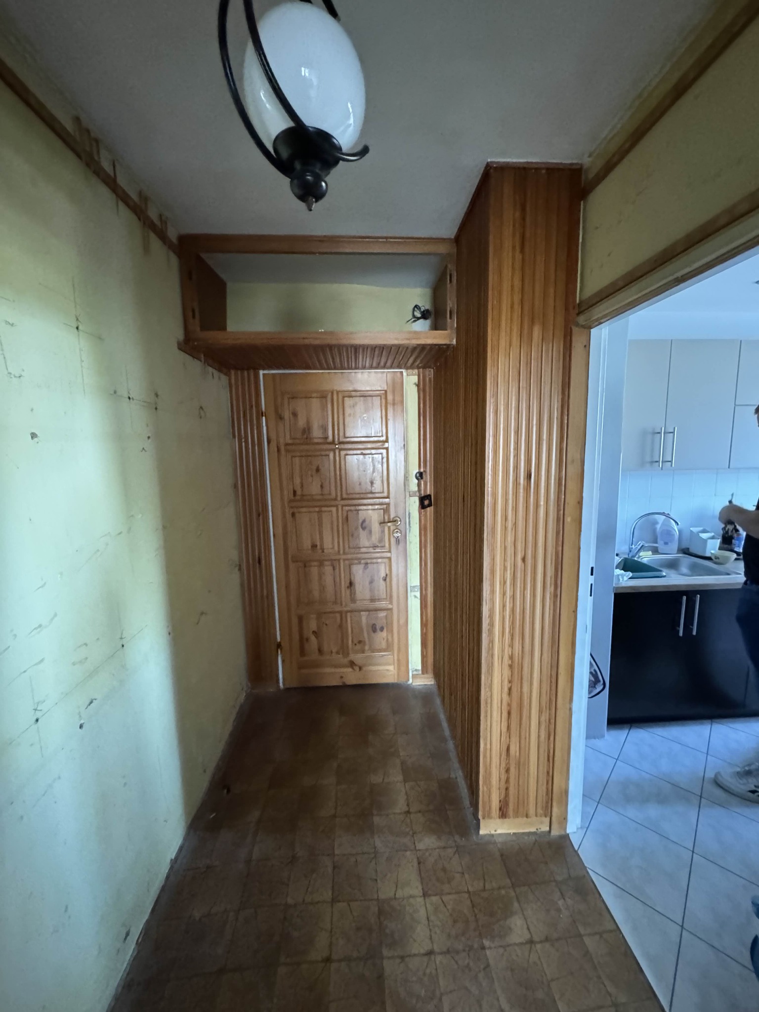 Korytarz przed odświeżeniem w Łęcznej: ściany z widocznymi śladami, drewniana boazeria i drzwi. Widoczny fragment kuchni w tle.