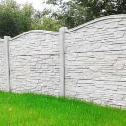 Betonowe ogrodzenie panelowe z dekoracyjnym wzorem kamienia, widok z poziomu trawnika. Estetyczne wykończenie posesji.