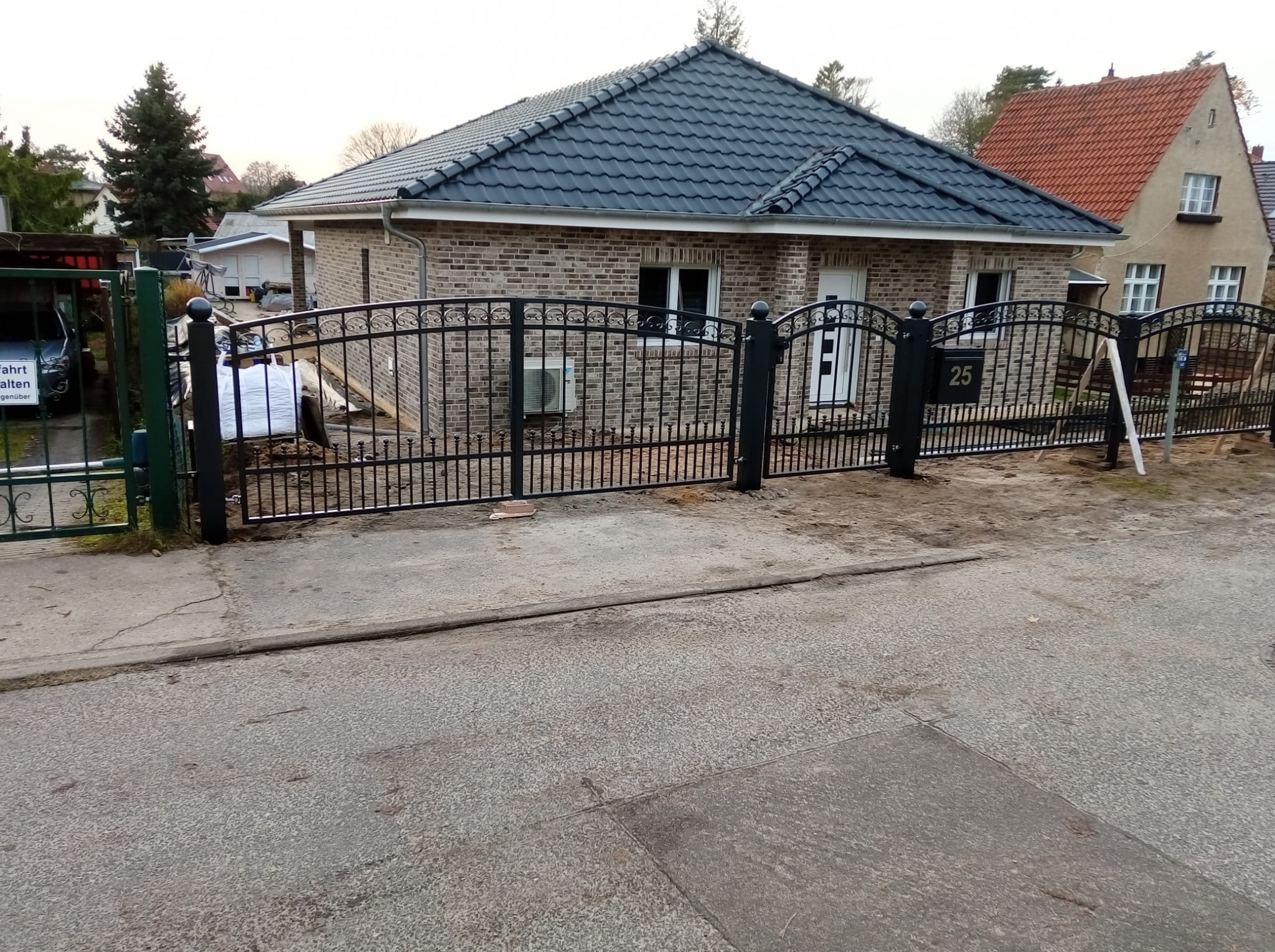 Eleganckie ogrodzenie metalowe z bramą, Namyślin. Czarna, łukowata konstrukcja przed domem z numerem 25. Widoczne ślady montażu.