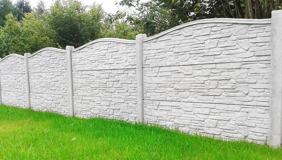 Betonowe ogrodzenie panelowe z dekoracyjnym wzorem kamienia, widok z poziomu trawnika. Estetyczne wykończenie posesji.