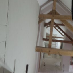 Jakub Michalski - Wnętrze w trakcie remontu: ściana z płyt gipsowych, drewniana konstrukcja dachu, widok na kolejne pomieszczenie. Prace wykończeniowe w budynku.