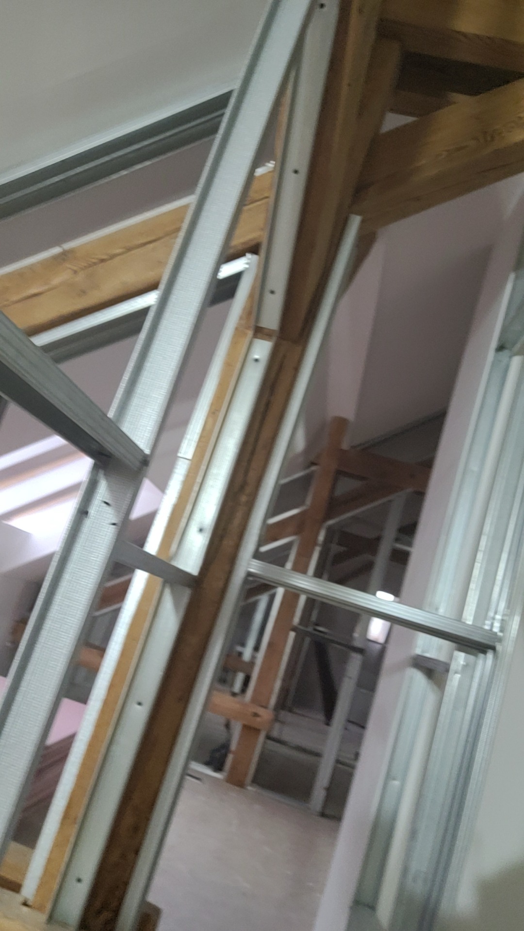 Konstrukcja szkieletowa z profili stalowych i drewnianych belek podczas budowy poddasza, widok od dołu. Metalowe elementy tworzą geometryczny wzór.