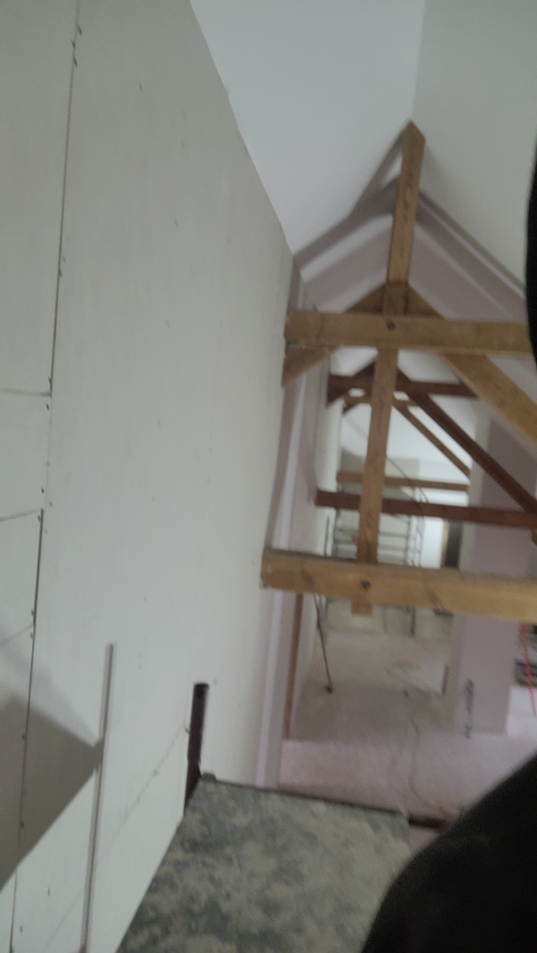 Wnętrze w trakcie remontu: ściana z płyt gipsowych, drewniana konstrukcja dachu, widok na kolejne pomieszczenie. Prace wykończeniowe w budynku.