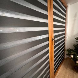 ROLETOWO MICHAŁ RYBCZYŃSKI - Zamknięte rolety dzień noc w drewnianej ramie okiennej, z widoczną częścią choinki w rogu, oświetlone naturalnym światłem.