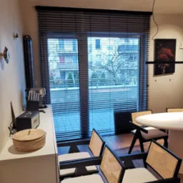 Ciemne żaluzje poziome w nowoczesnym wnętrzu z białymi meblami i widokiem na miasto. Minimalistyczny design, stonowana kolorystyka, naturalne światło.