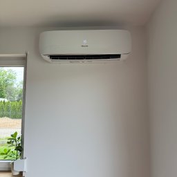 Air Balance Hubert Górka - Biała klimatyzacja Hisense zamontowana na białej ścianie w jasnym pomieszczeniu, obok okna z rośliną. Widoczny wyświetlacz z temperaturą 16 stopni.