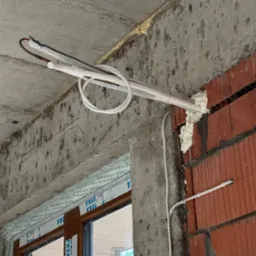 Montaż instalacji z przewodami w białej izolacji, prowadzonej pod sufitem w surowym stanie, z widocznymi elementami konstrukcyjnymi budynku.