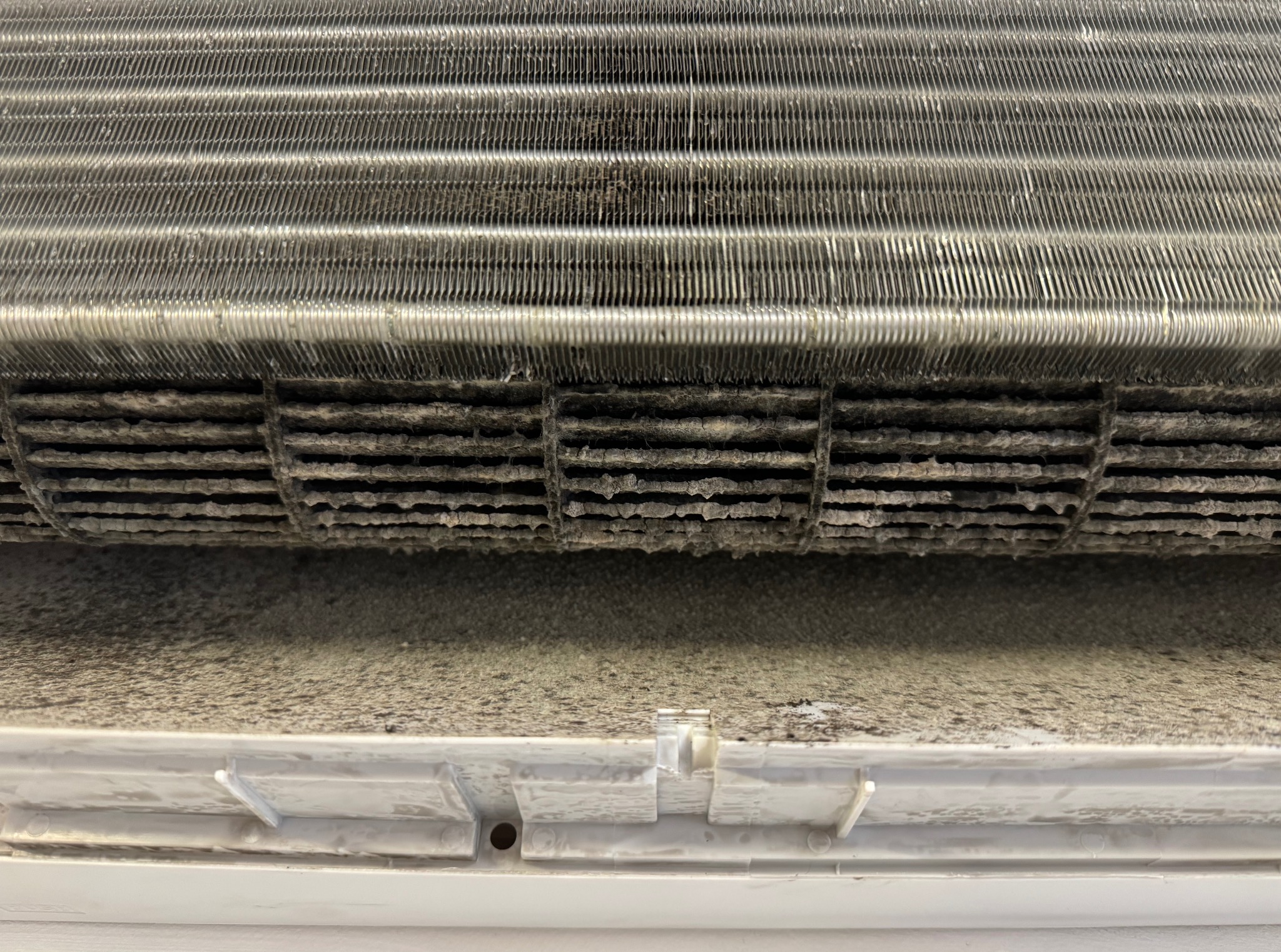 Zanieczyszczony, zakurzony filtr klimatyzacji, widoczne drobinki kurzu na lamelach i obudowie. Konieczność czyszczenia i serwisu.