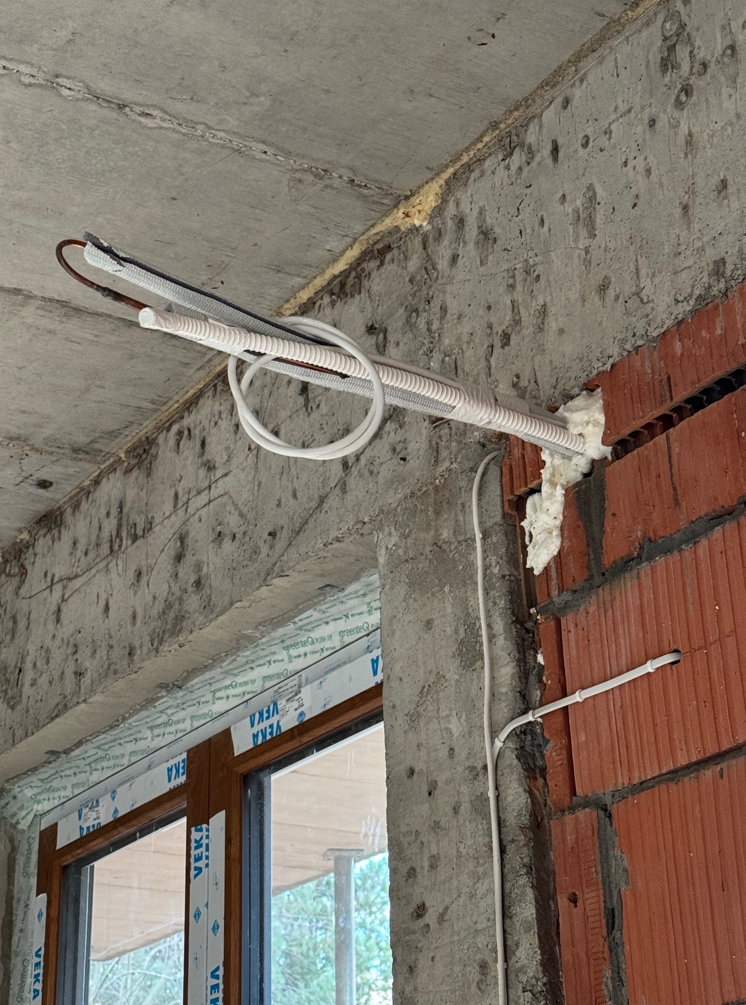 Montaż instalacji z przewodami w białej izolacji, prowadzonej pod sufitem w surowym stanie, z widocznymi elementami konstrukcyjnymi budynku.