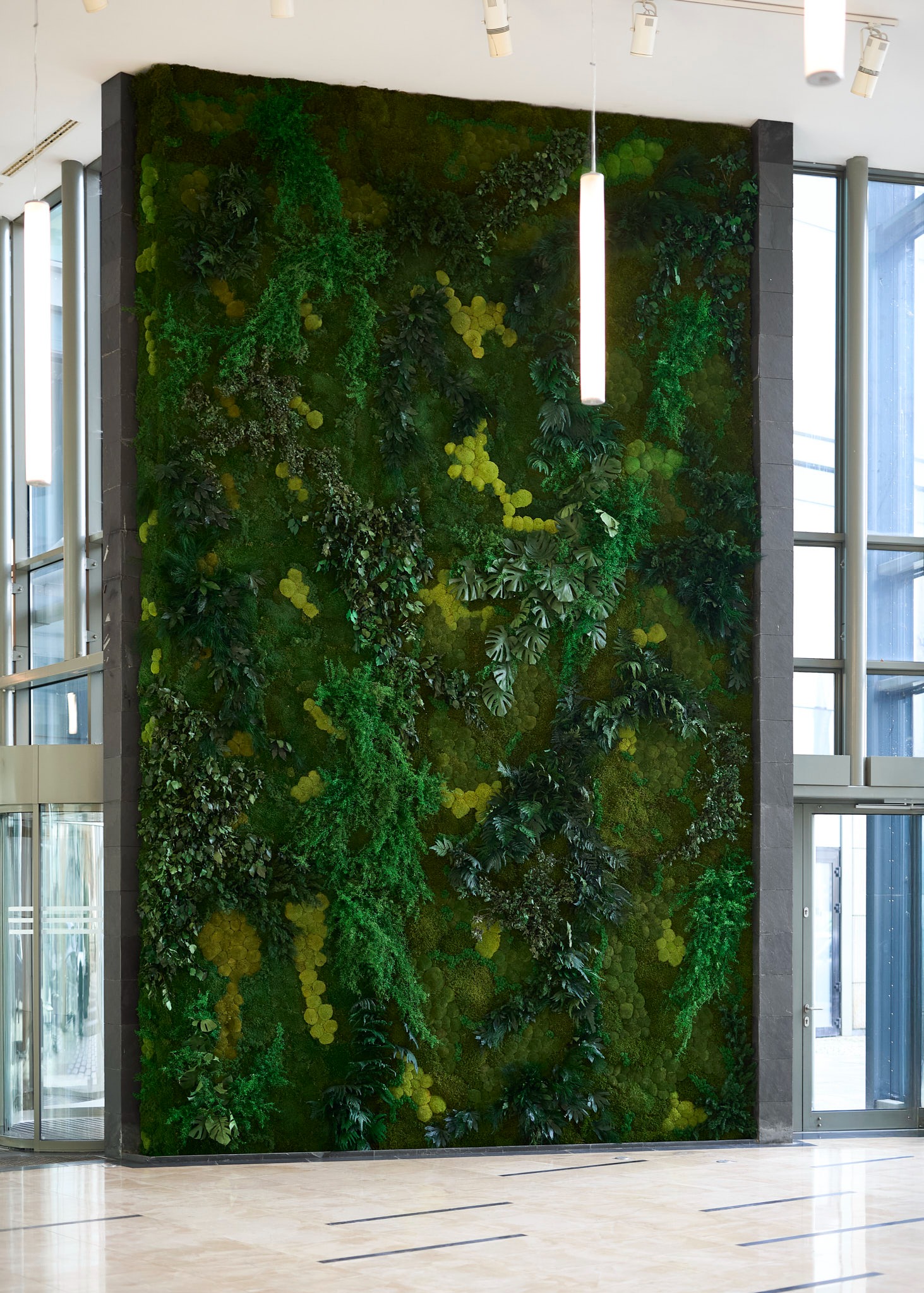 Wertykalny ogród z mchu i roślin w nowoczesnym biurze, oświetlony lampą wiszącą. Zielona ściana jako element dekoracyjny w przestrzeni biurowej.