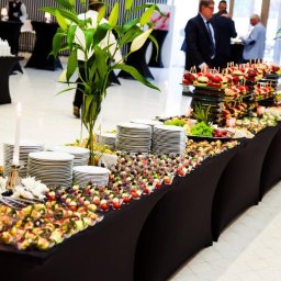 u.studio Paulina Miziewicz - Elegancko zastawiony stół cateringowy z przekąskami, dekoracjami kwiatowymi i świecami, gotowy na przyjęcie. Widoczni goście w tle.