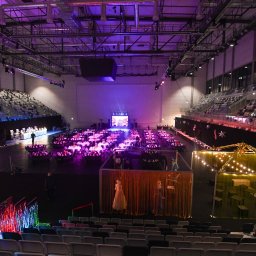 u.studio Paulina Miziewicz - Widok z góry na halę widowiskową przygotowaną na galę. Ustawione okrągłe stoły, dekoracje świetlne i ścianki działowe. Scena w tle. Fioletowe oświetlenie.