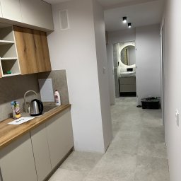 New Vision Pro Artur Froncz - Nowoczesne wykończenie wnętrza mieszkania w Kielcach: kuchnia z drewnianymi akcentami i widok na łazienkę z okrągłym lustrem.