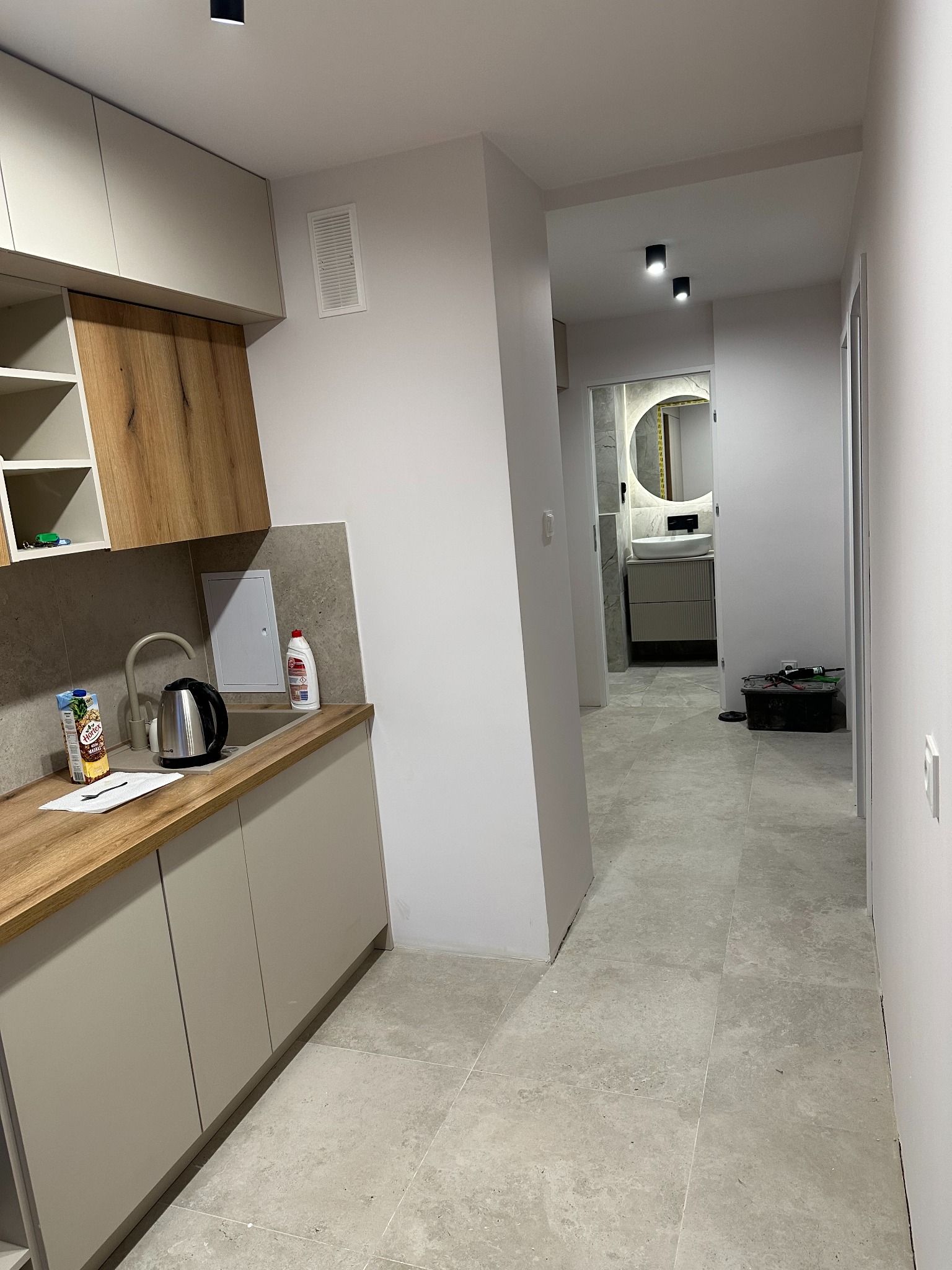 Nowoczesne wykończenie wnętrza mieszkania w Kielcach: kuchnia z drewnianymi akcentami i widok na łazienkę z okrągłym lustrem.