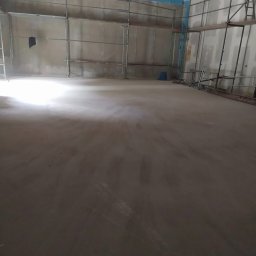 RPM Center Sp. z.o.o. - Wnętrze w trakcie szpachlowania z rusztowaniami. Sufit zabezpieczony folią. Podłoga wylewka. Ściany przygotowane pod malowanie. Widok na dużą powierzchnię w trakcie prac wykończeniowych.