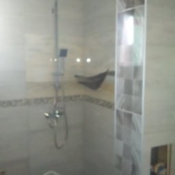 Norbert Stępień - Wykończona łazienka z kabiną prysznicową typu deszczownica i płytkami w odcieniach bieli i szarości. Widoczny fragment drabiny.