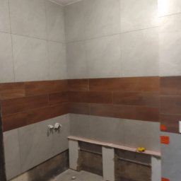 Norbert Stępień - Łazienka w trakcie prac wykończeniowych: ułożone płytki ścienne w odcieniach szarości i brązu, widoczne narzędzia, przygotowane podłoże pod dalsze prace.