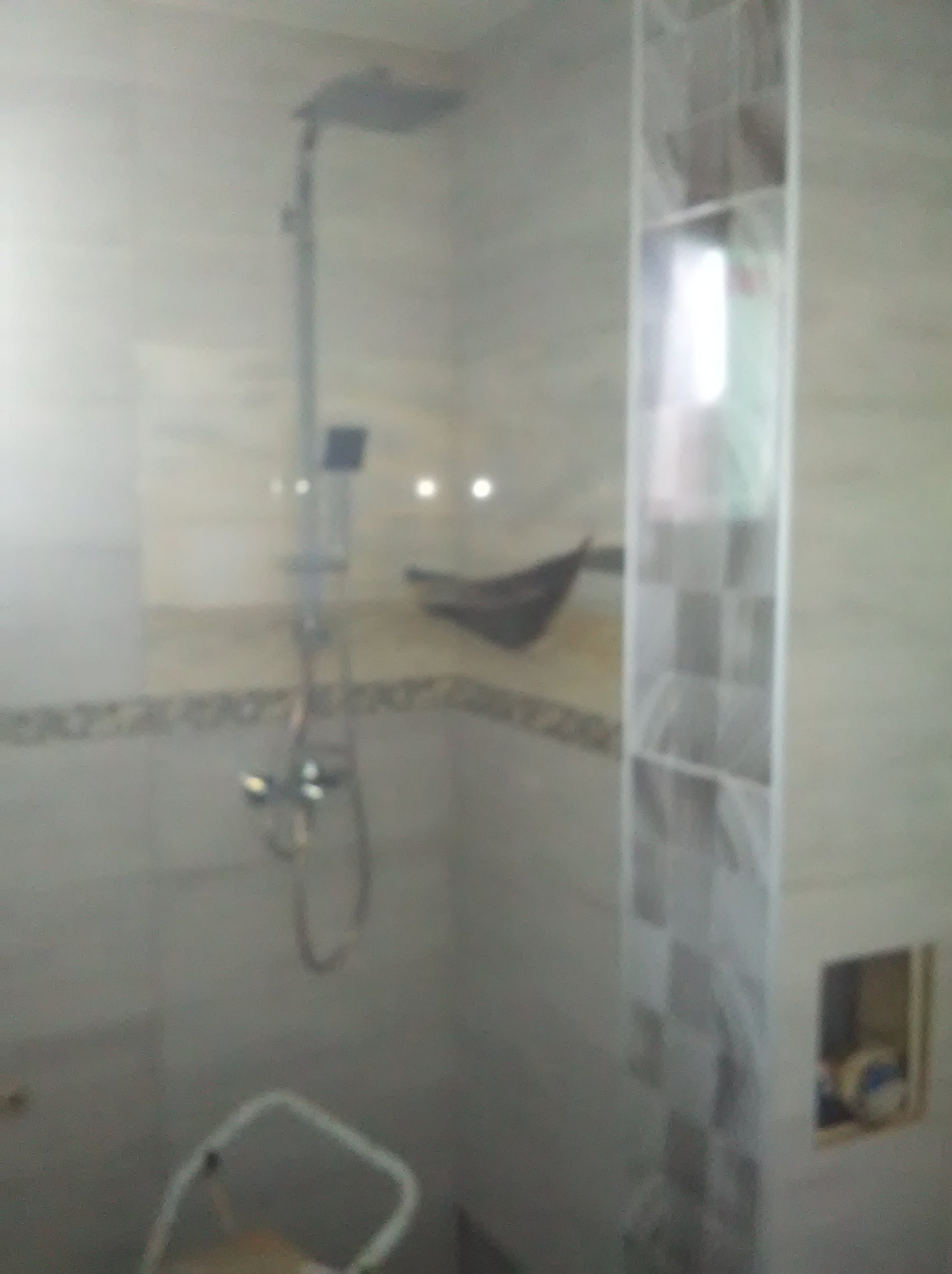 Wykończona łazienka z kabiną prysznicową typu deszczownica i płytkami w odcieniach bieli i szarości. Widoczny fragment drabiny.