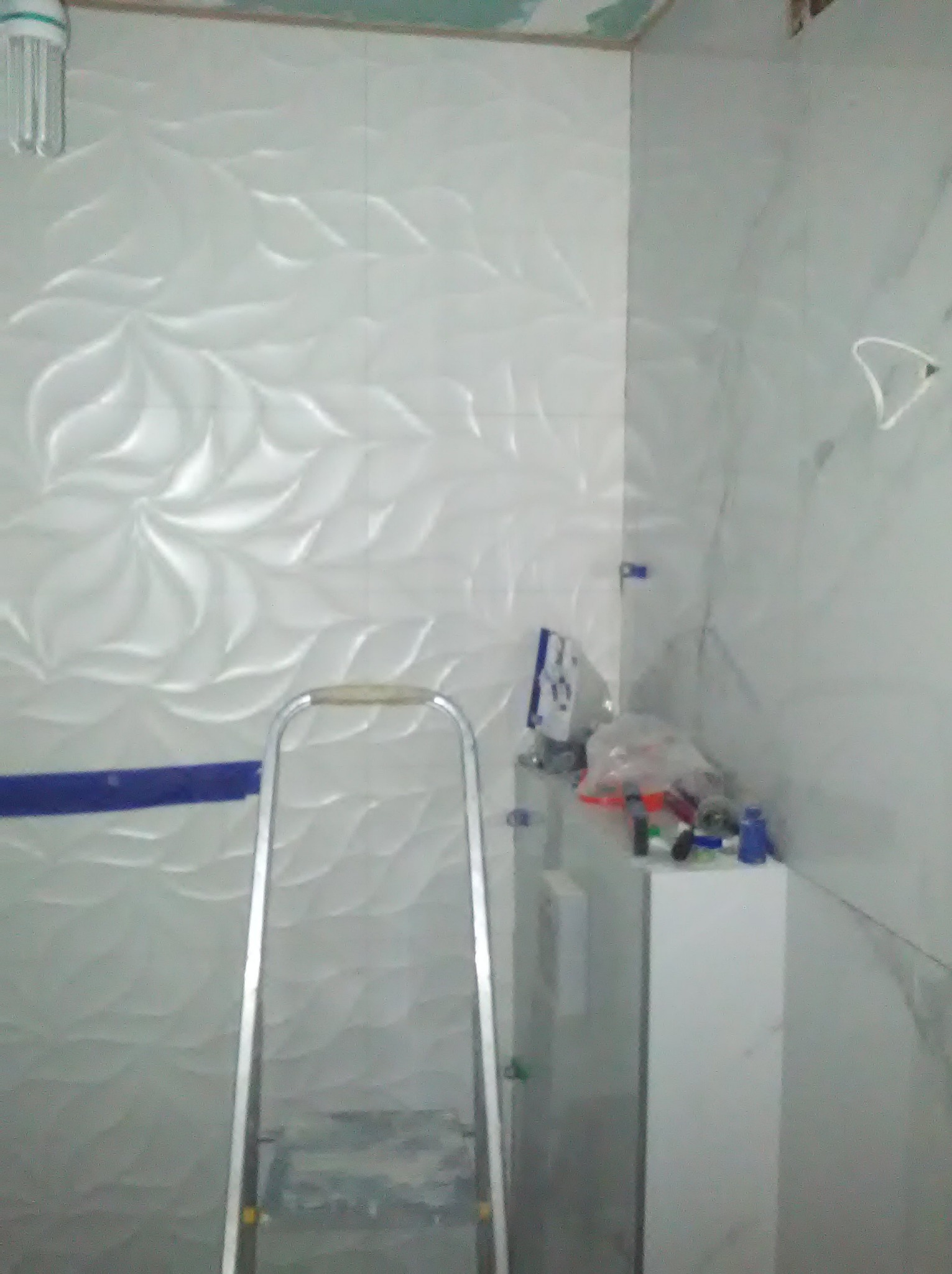 Białe, wzorzyste płytki w łazience, częściowo ułożone. Widoczna drabina i akcesoria glazurnicze. Etap wykończeniowy, z bliska.