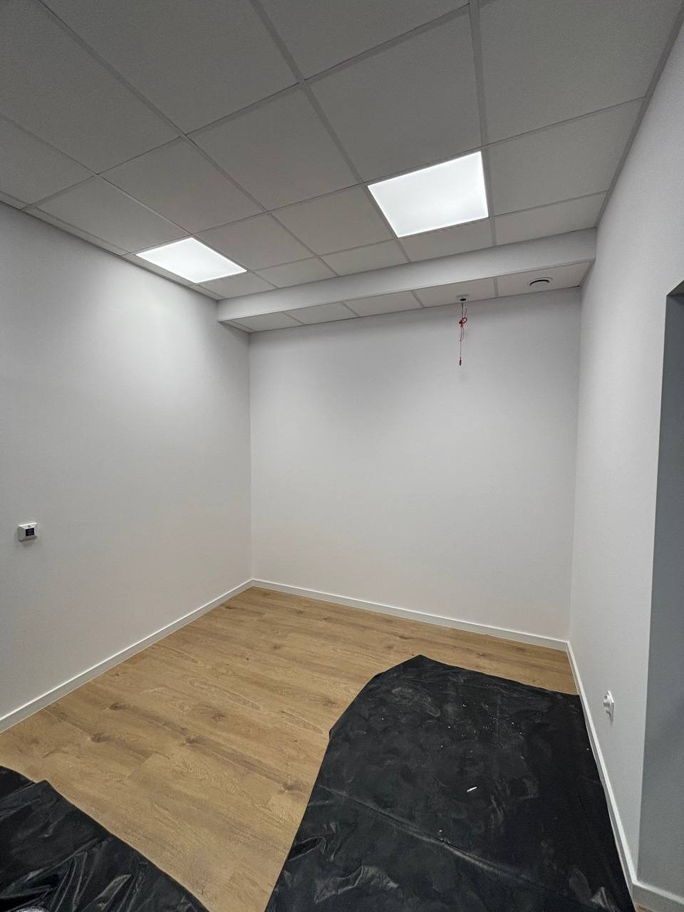 Wnętrze pokoju po malowaniu ścian na biało z panelami na podłodze. Na podłodze folia ochronna. Sufit podwieszany z oświetleniem LED.