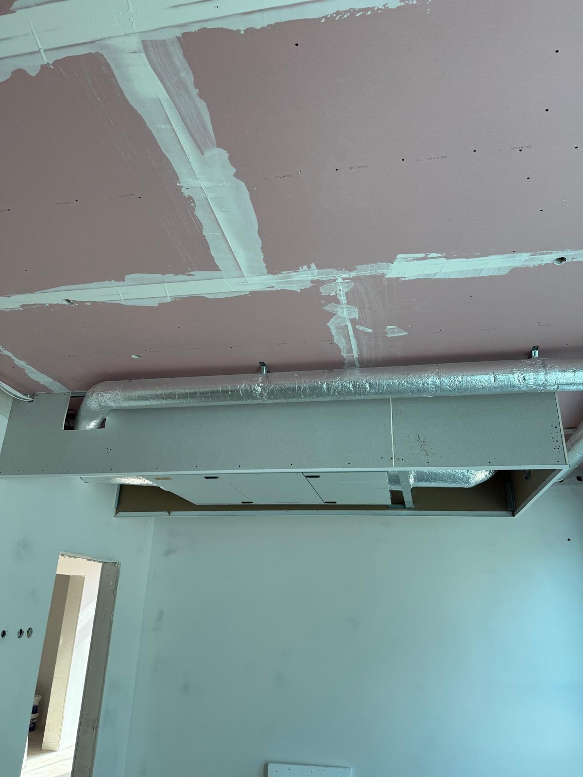 Montaż sufitu z płyty gipsowej z widoczną instalacją wentylacyjną; na płycie widoczne łączenia po szpachlowaniu, ściany przygotowane do malowania, widoczny fragment drzwi.