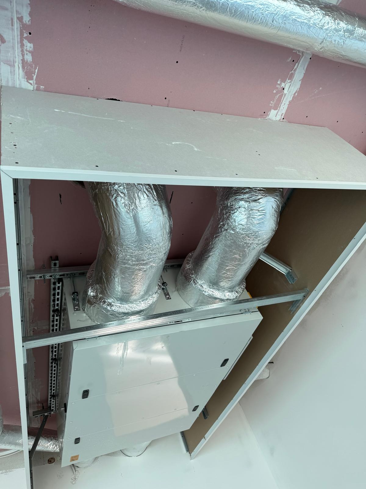 Montaż systemu wentylacji z płyt g-k w Gdańsku. Widoczne izolowane rury i biała obudowa. Ściany z płyt kartonowo-gipsowych w kolorze różowym.