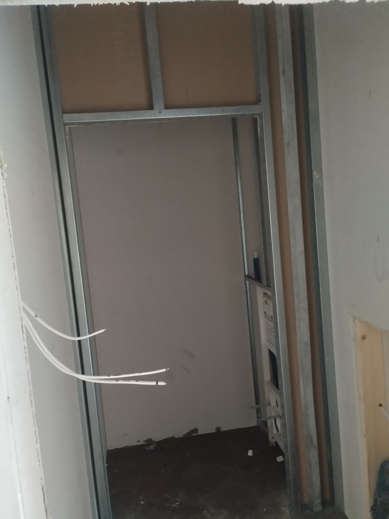 Konstrukcja metalowa z płytą GK w trakcie montażu, widoczne przewody elektryczne i elementy instalacji sanitarnej wewnątrz. Surowy stan wykończenia wnętrza.