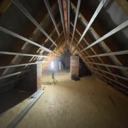 Montaż stelażu pod płyty G-K na poddaszu w Strzelinie. Widoczne profile metalowe, drewniana konstrukcja dachu i oświetlenie robocze. Prace wykończeniowe.