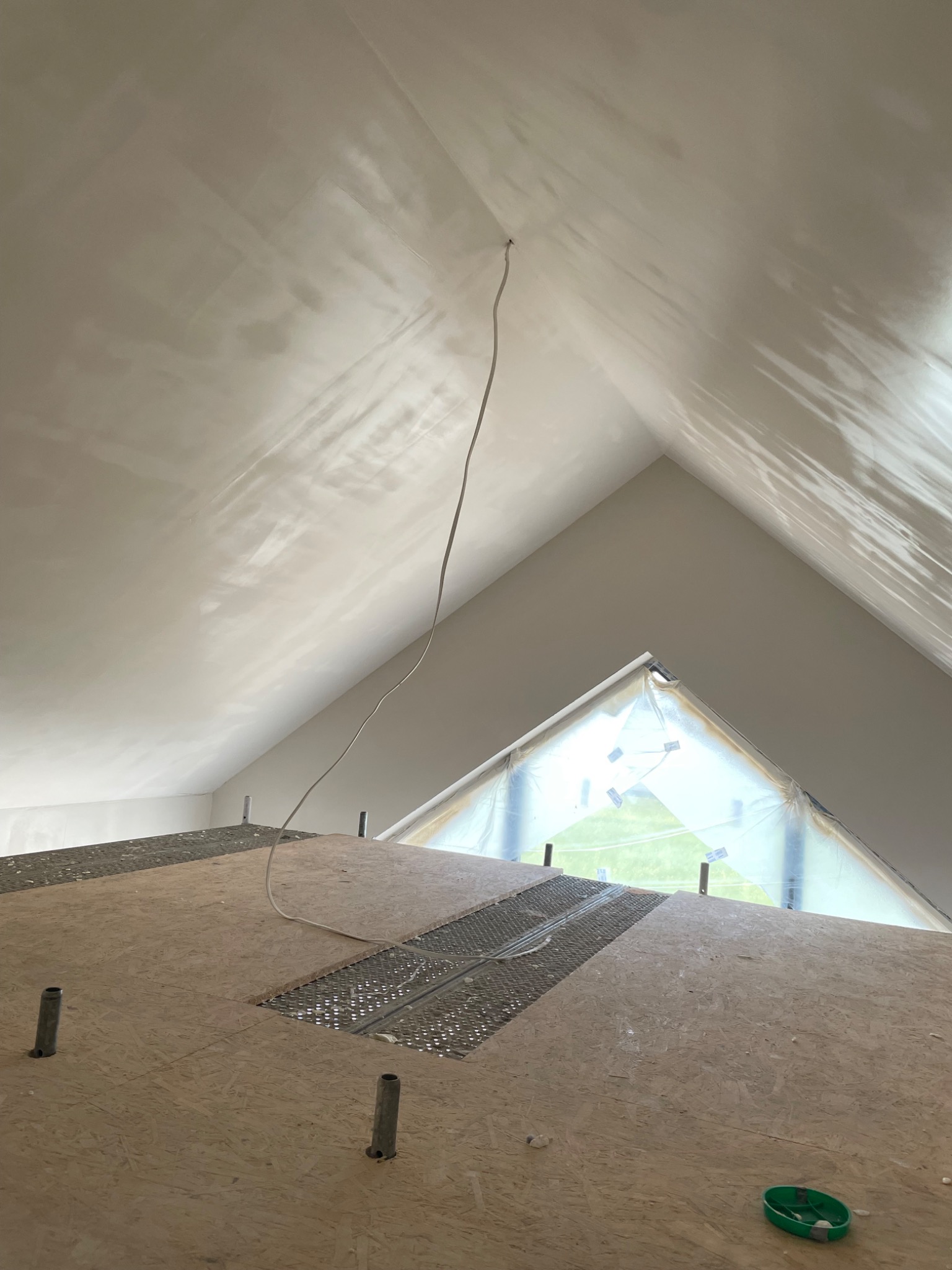 Poddasze ze świeżo wykończoną, jasną powierzchnią sufitu, zabezpieczonym oknem i fragmentem podłogi z elementami konstrukcyjnymi.