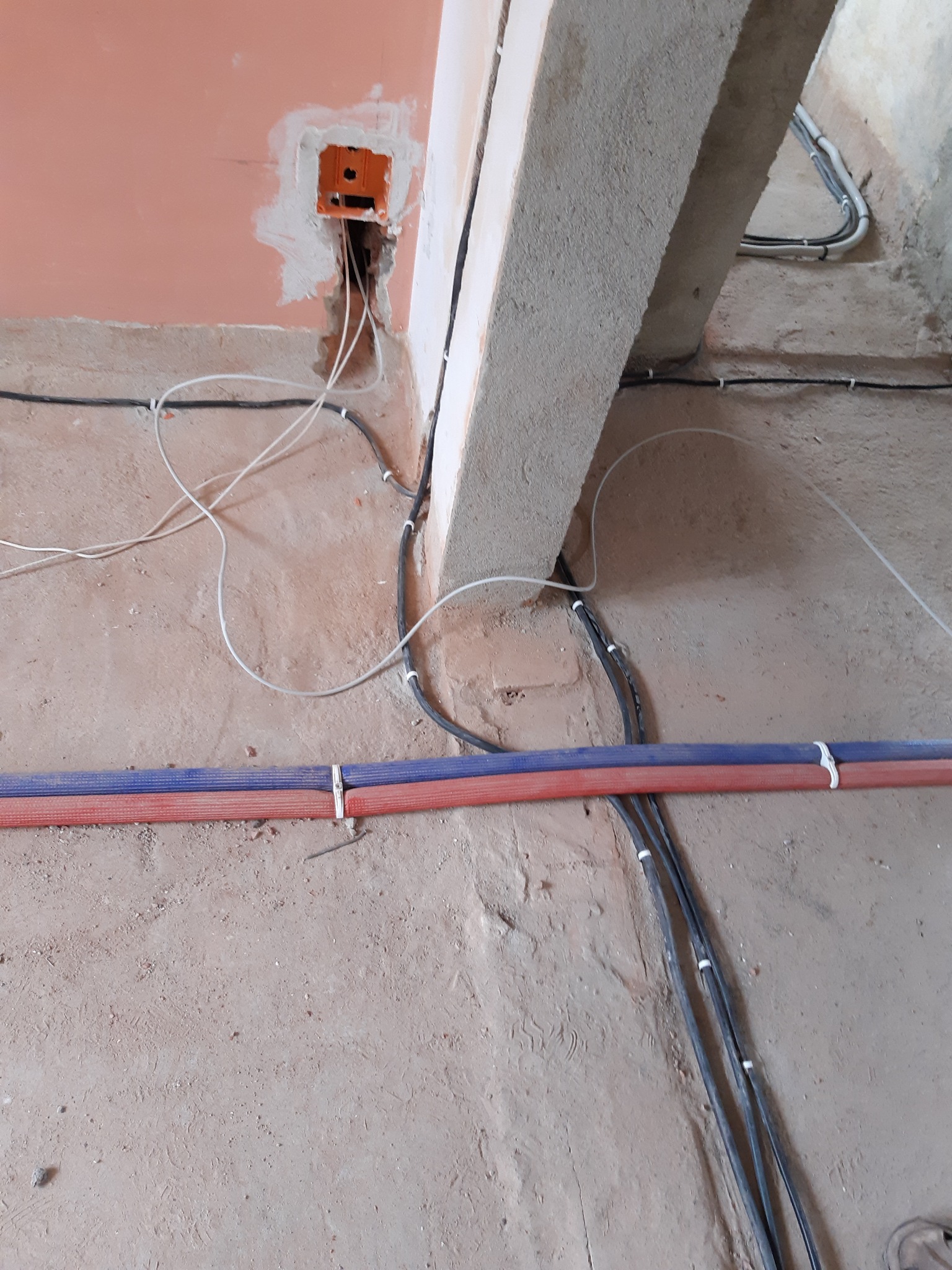 Wnętrze w trakcie prac instalacyjnych: kable elektryczne prowadzone wzdłuż ściany i podłoża, widoczna puszka instalacyjna w ścianie, fragment konstrukcji budynku.