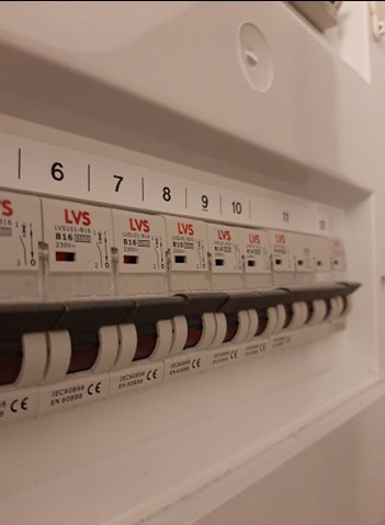 Rozdzielnica elektryczna z bezpiecznikami LVS B16, numery 6-12, w białej obudowie. Widoczne oznaczenia i certyfikaty CE. Ujęcie z dołu.