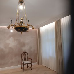 Wiesław Cygan Firma Remontowa - Eleganckie wnętrze z parkietem w jodełkę, krzesłem i ozdobnym żyrandolem. Ściana z efektem chmur i jasne zasłony w tle. Całość w stonowanej kolorystyce.