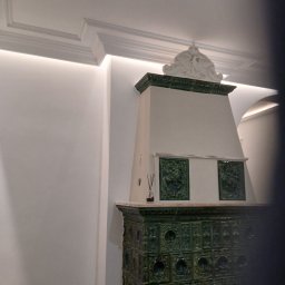 Wiesław Cygan Firma Remontowa - Stylowy, odnowiony piec kaflowy w odcieniach zieleni, z dekoracyjnymi kaflami i białym wykończeniem, w jasnym wnętrzu z subtelnym oświetleniem.