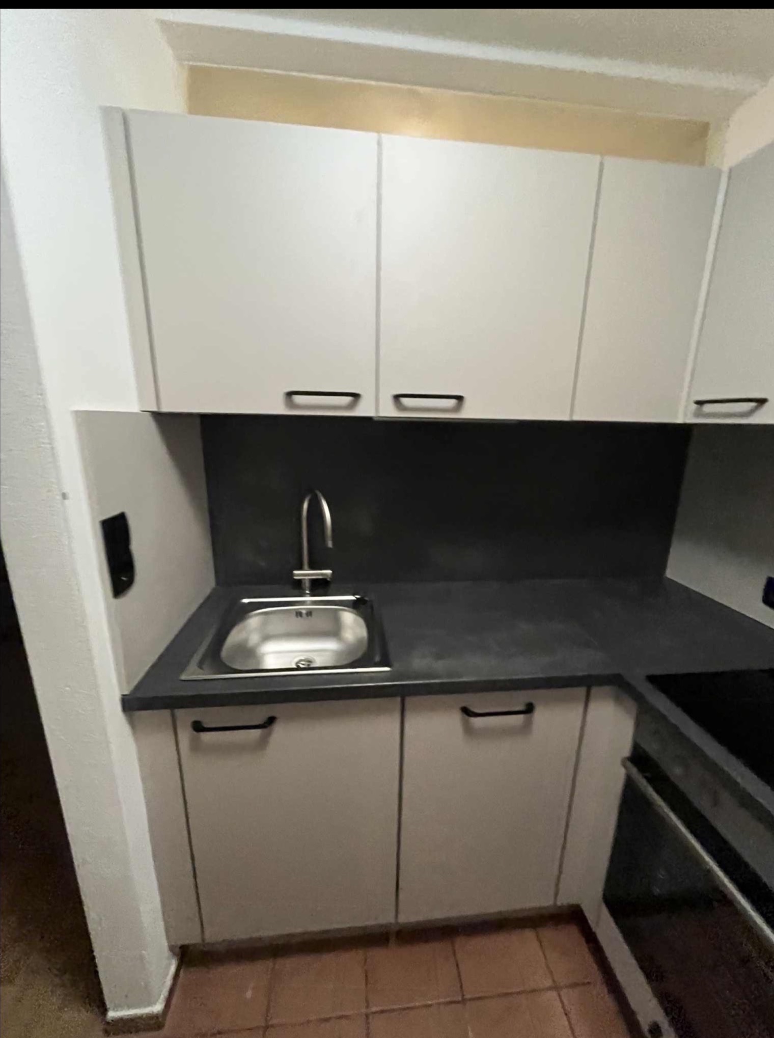 Jasna zabudowa kuchenna z ciemnym blatem i zlewozmywakiem. Widoczne szafki górne i dolne z minimalistycznymi uchwytami. Ujęcie na fragment kuchni po remoncie.