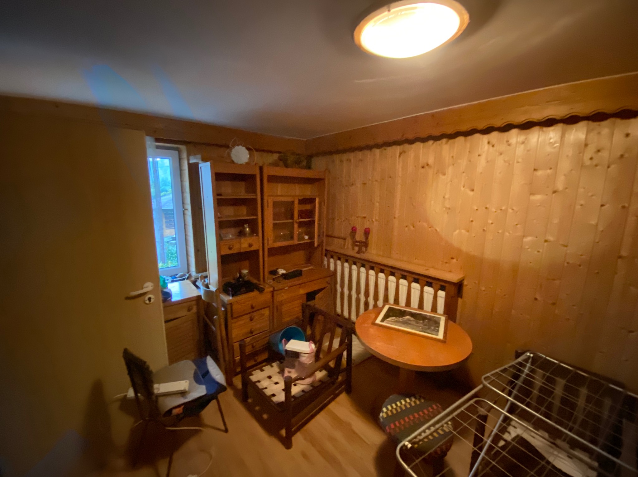 Pokój z drewnianą boazerią, meblami i suszarką na pranie. Widoczne ślady użytkowania, sugerujące przygotowanie do opróżniania mieszkania.